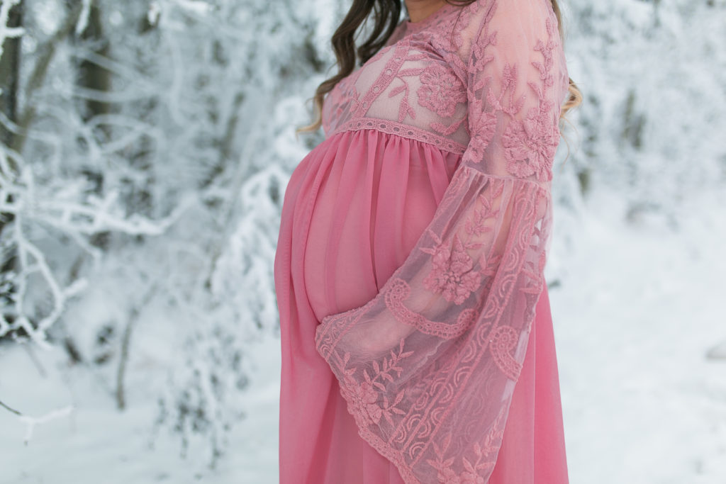 Pregnant woman in pink maternity dress surrounded by snow and hoar frost
