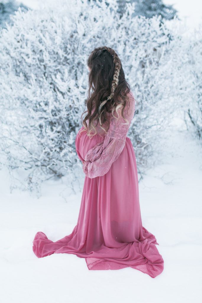 Pregnant woman in pink maternity dress surrounded by snow and hoar frost