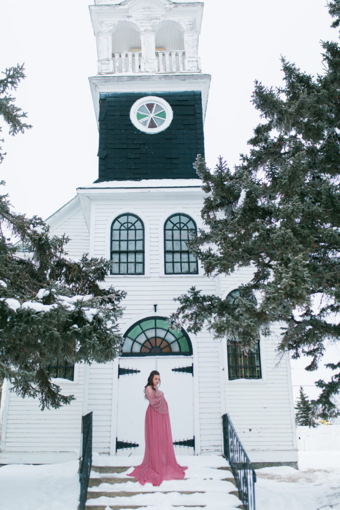 Pregnant woman in pink maternity dress in front of white church